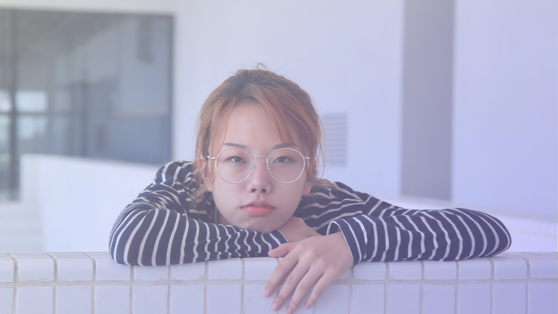Women in a striped shirt resting her head on her arms while she leans against a wall.