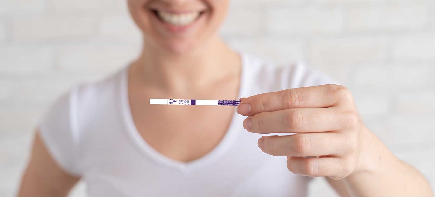 Woman smiling and holding a Proov test strip.