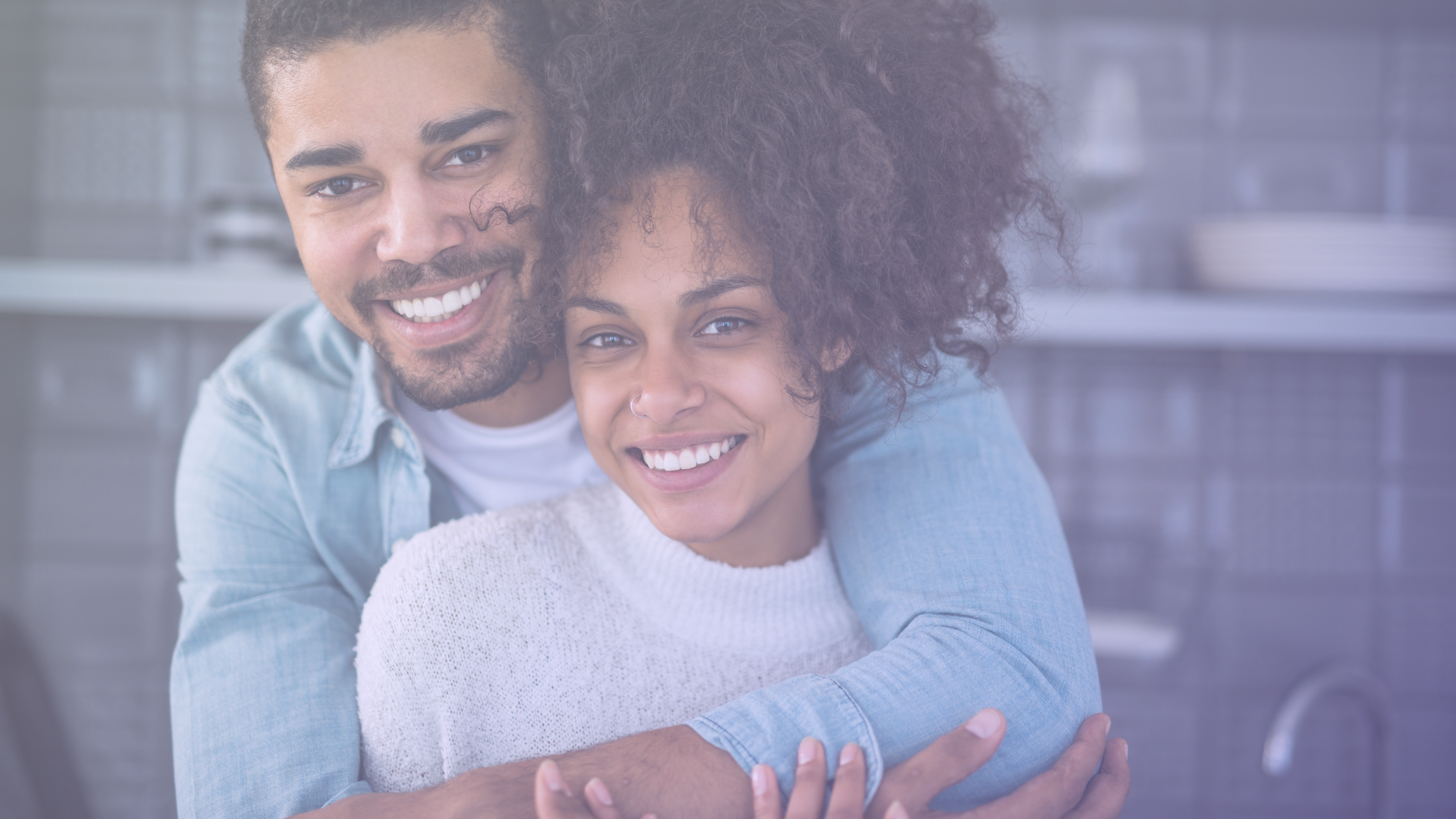 An image of a man and woman smiling, with the man embracing the woman from behind.