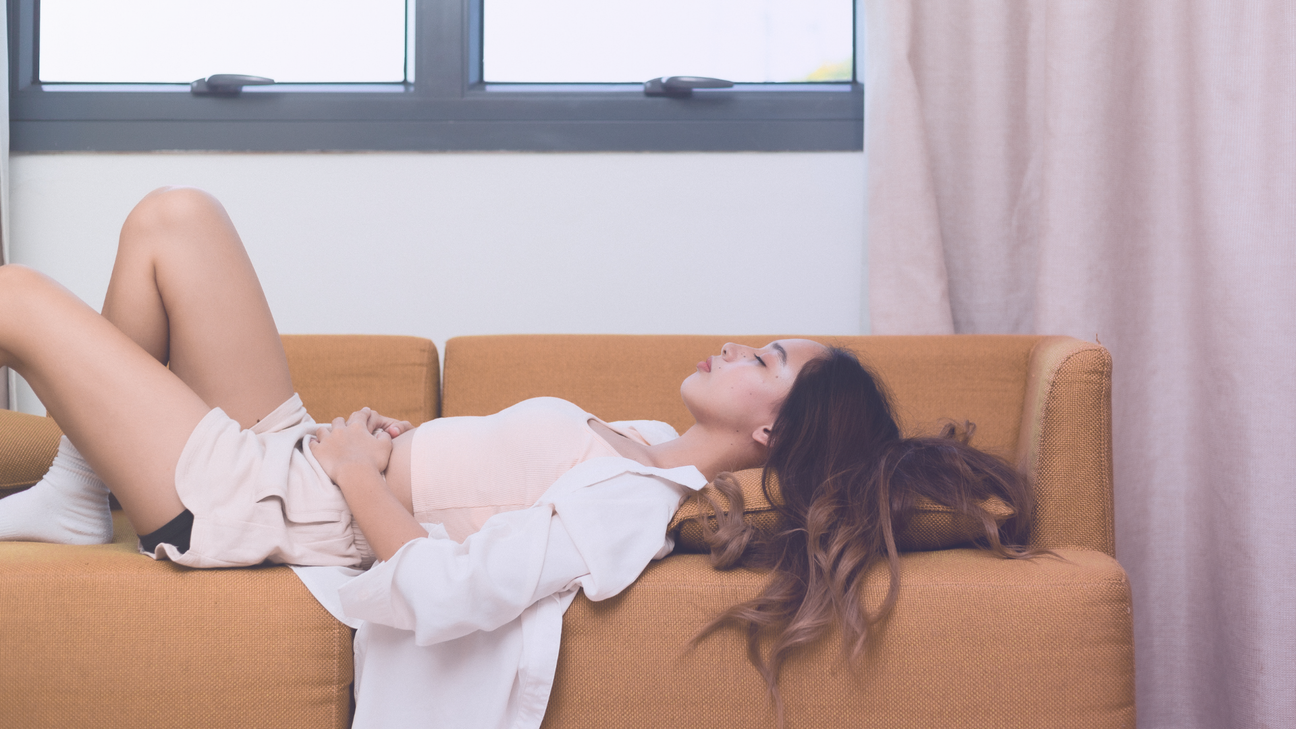 Woman with menstrual cramps holding her stomach and laying on the couch
