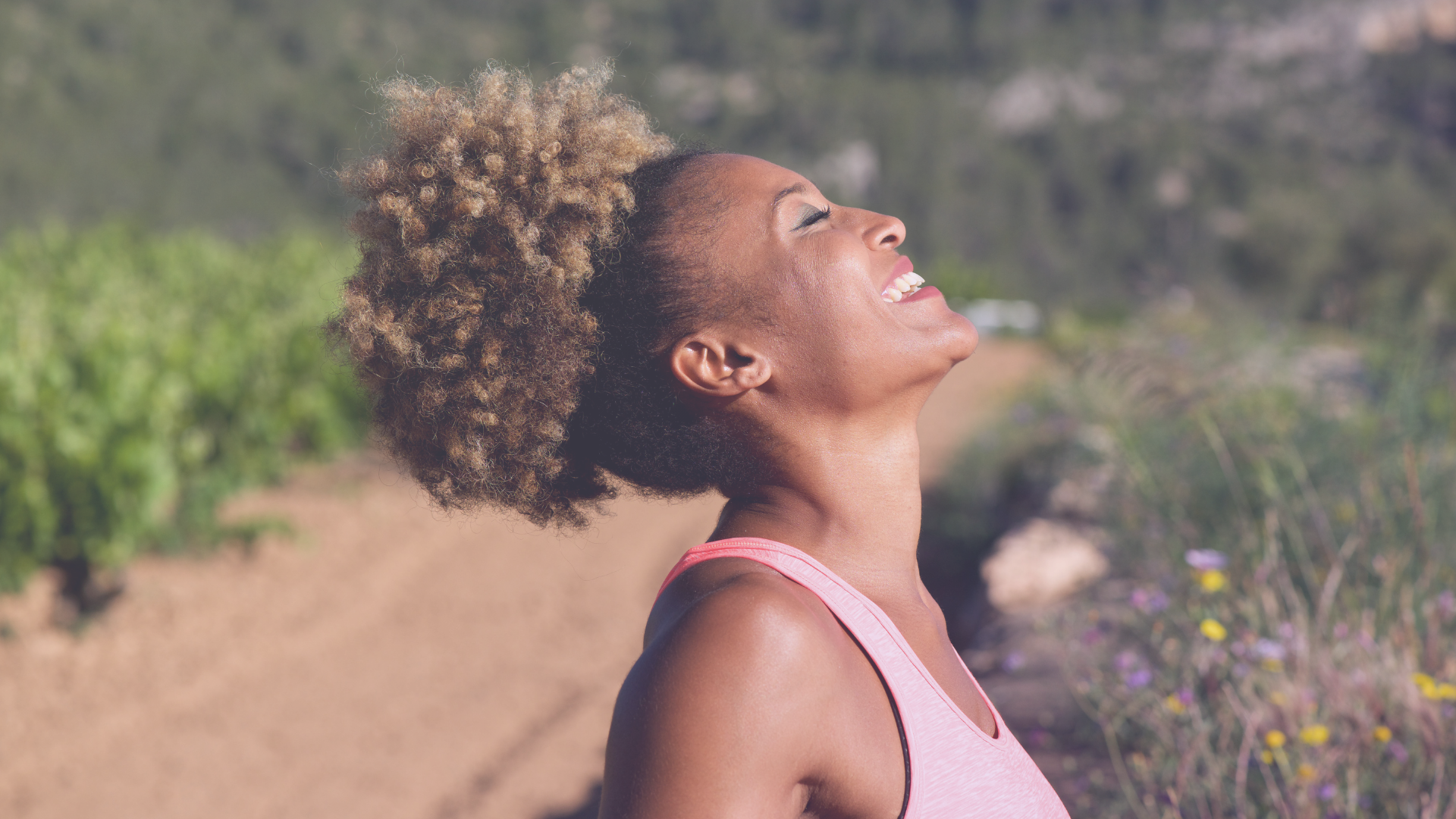 Woman tilting her head back and smiling with her eyes closed, in the outdoors