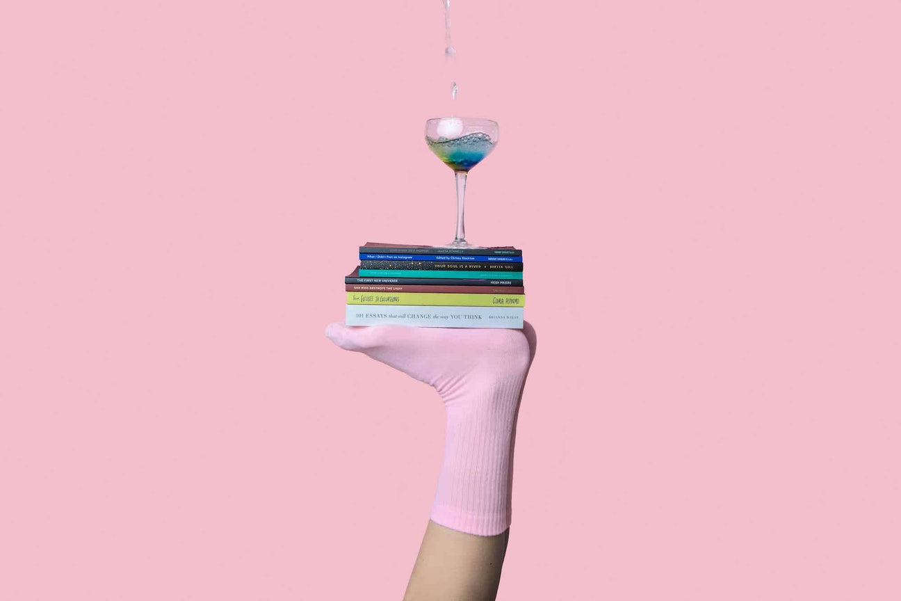 Feet with pink socks balancing a stack of books and a glass of liquid.