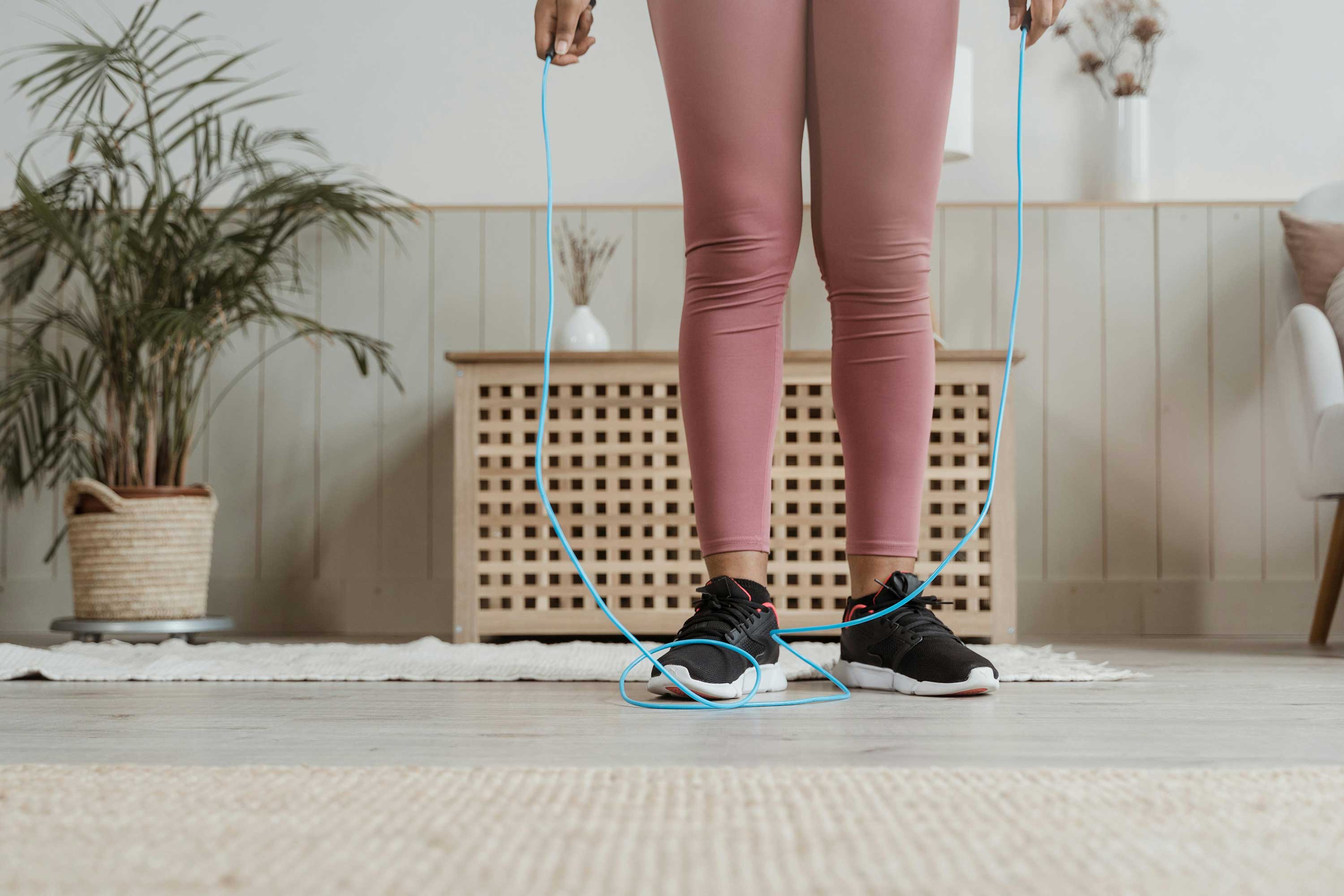 Woman in pink leggings and jogging shoes, holding a jump rope. 